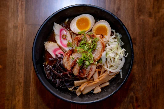 A bowl of ramen with chashu pork, a soft egg, bamboo shoots and fish cake